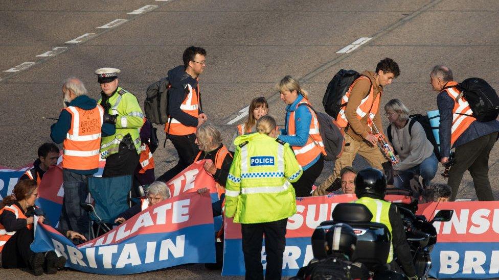 Group of protestors holding banners sitting on the M25 motorway speaking to police.