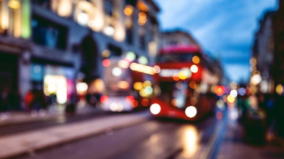 A bus approaches a stop on a London street at night