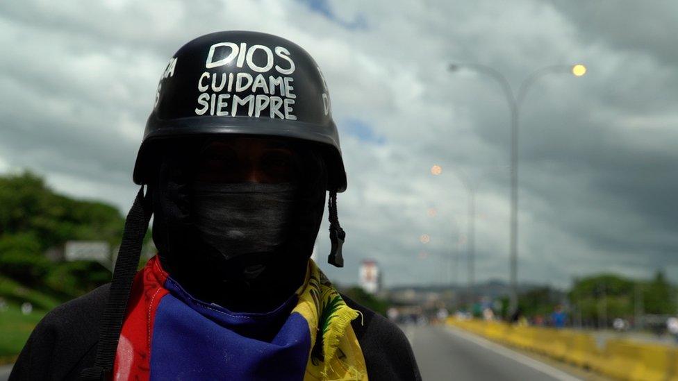 A protester with a helmet reading "God, protect me always" in Caracas