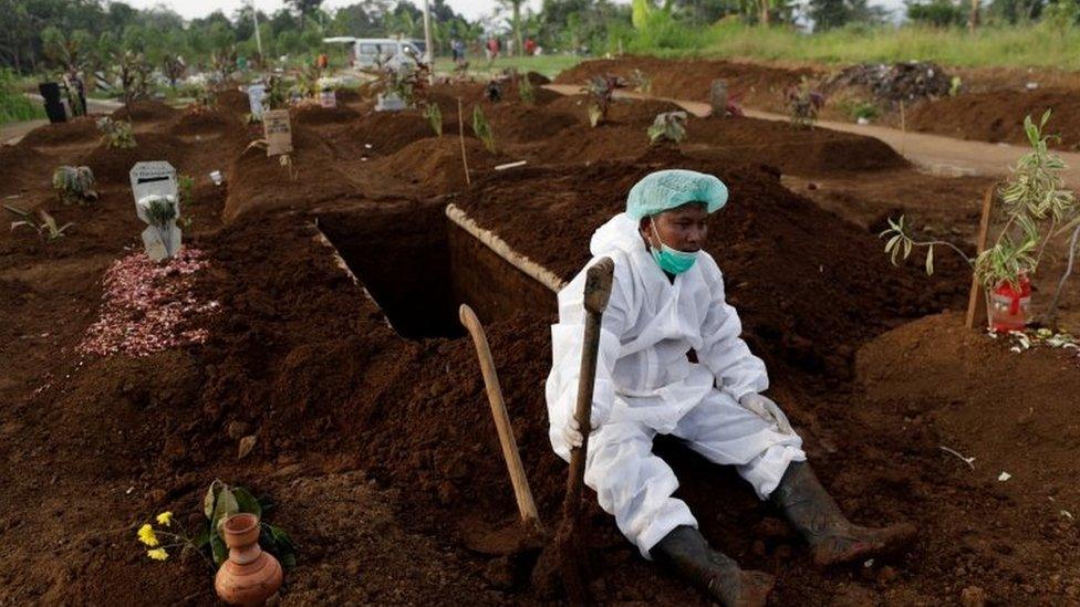 A gravedigger wearing personal protective equipment rests