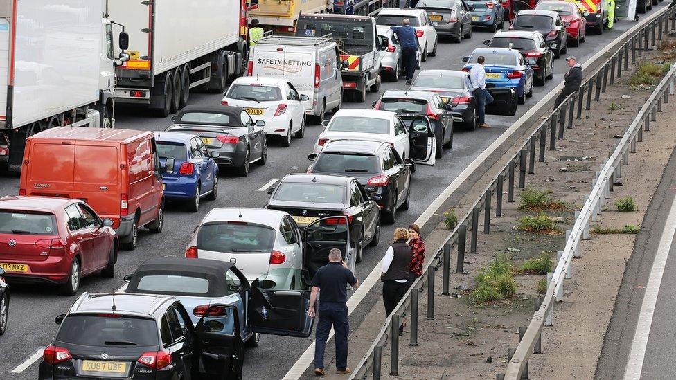 Motorists talk on the side of the road next to stranded cars