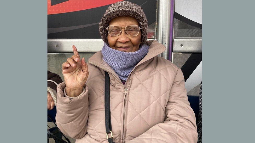 Ms Johnson-Martin sat at a bus stop wearing a scarf and a hat