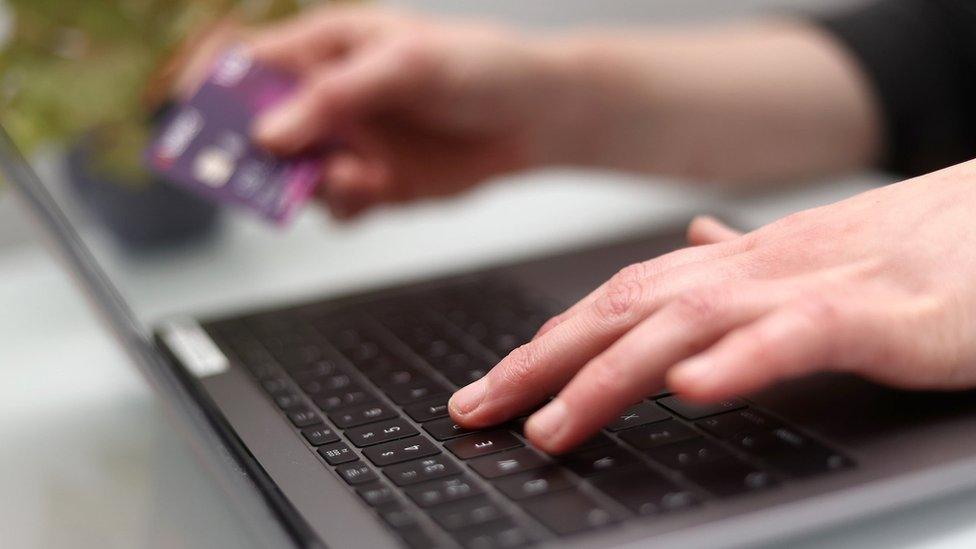 Someone typing on a computer with their left hand and holding a bank card with their right hand