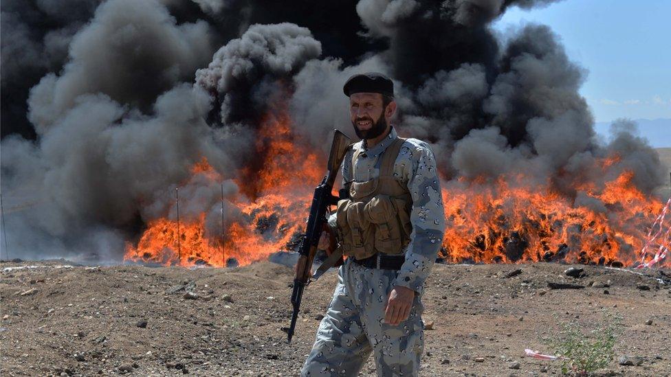 An Afghan security personnel stands guard as seized drugs and alcoholic drinks burn on the outskirts of Jalalabad