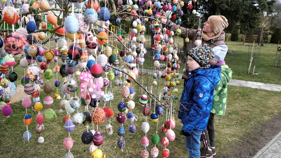 People look at garlands of multi-coloured eggs hung on trees in Seduva, Lithuania, 11 April 2022. There are about 11,000 Easter eggs decorating an avenue in town.