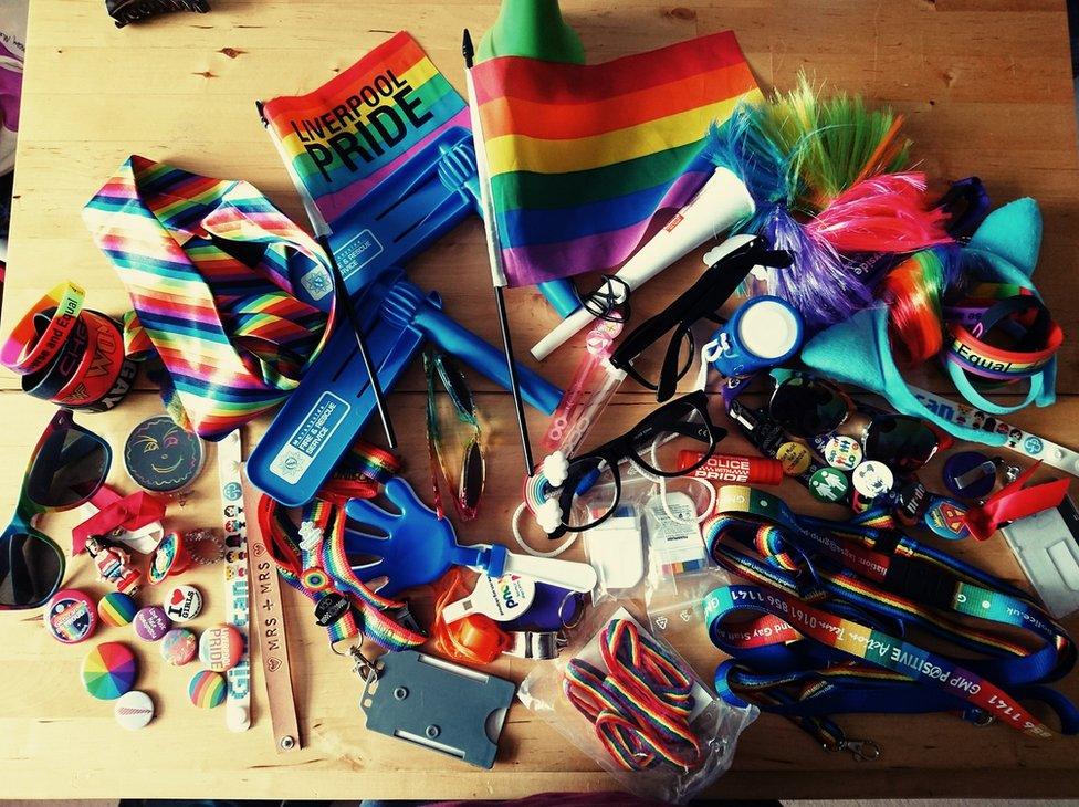 A table covered in rainbow-coloured flags, ties, buttons, glasses and more