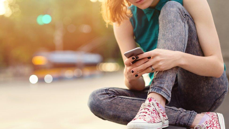 A girl sat on a wall using her phone