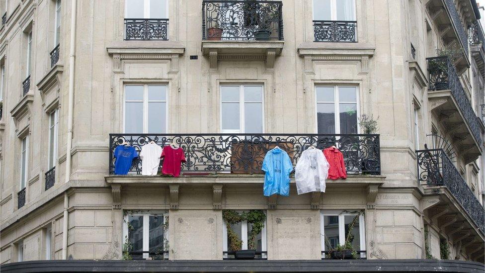 T-shirts and coats in colours of French flag hang from a balcony in Paris