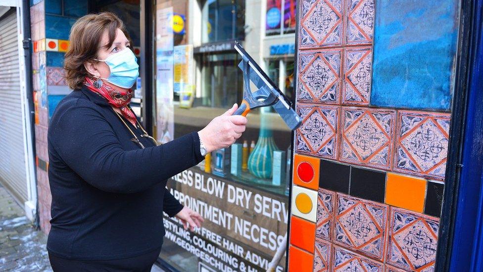A woman cleans the windows of her hairdressing salon