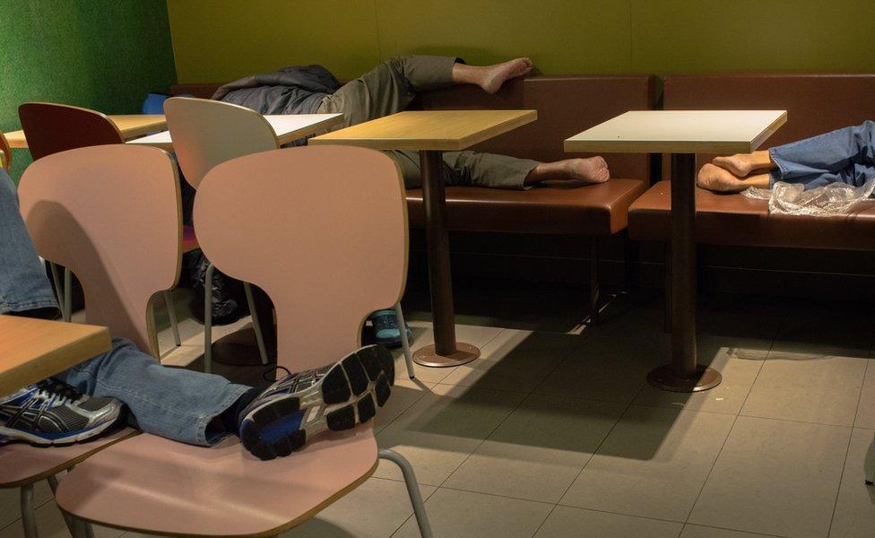 People lying down to sleep on seating in McDonald's