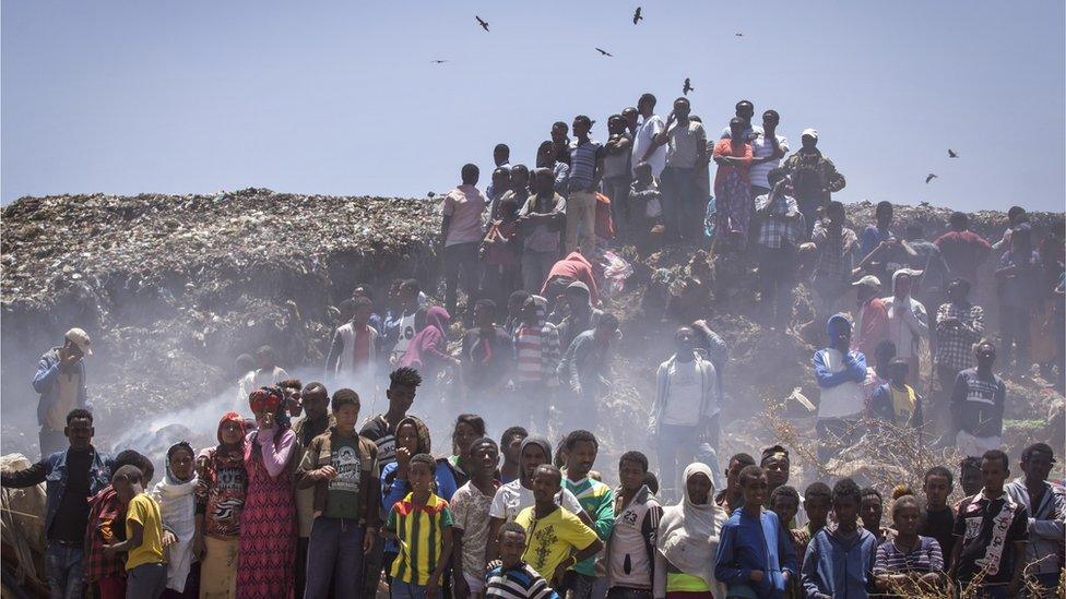 Residents look on as rescue efforts take place at the scene of a garbage landslide,