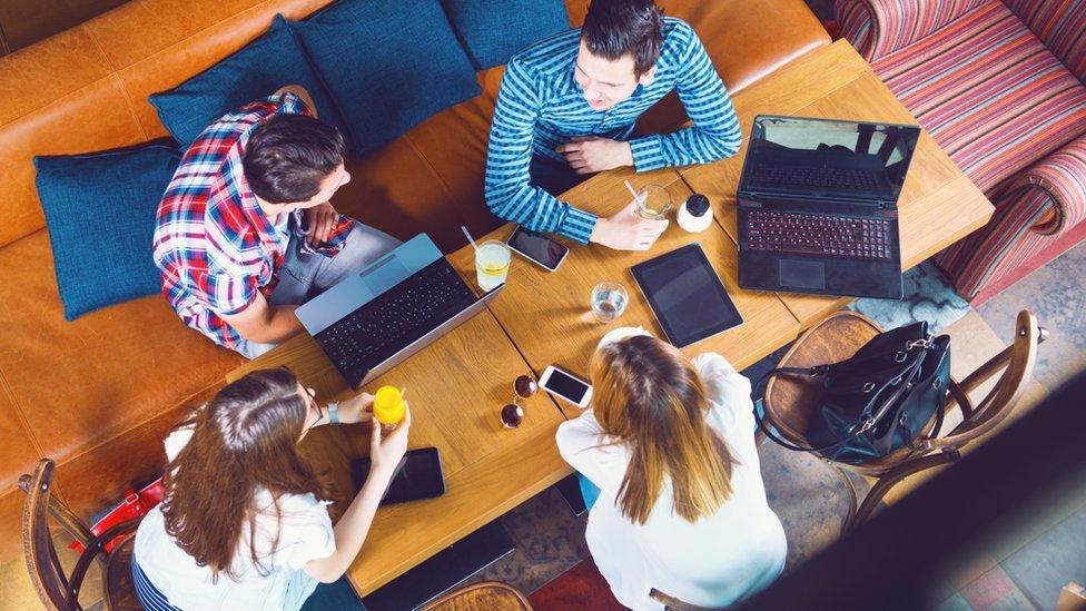 people in cafe, laptops and phones on tables