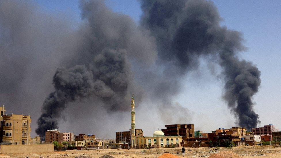 A man walks while smoke rises above buildings after aerial bombardments during clashes between the paramilitary Rapid Support Forces (RSF) and the army in Khartoum, Sudan - May 2023