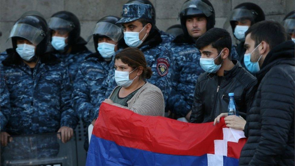 Demonstrators hold the national flag as law enforcement officers stand guard in front of the building of the National Assembly