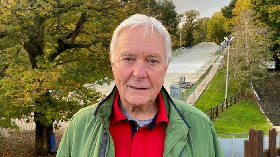 A man with white hair standing in front of a dry ski slope