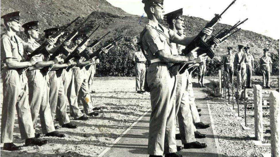 Soldiers present arms beside open graves