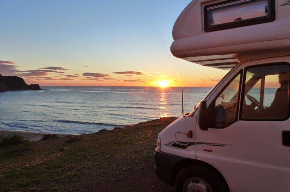 Campervan parked beside sea and sunset