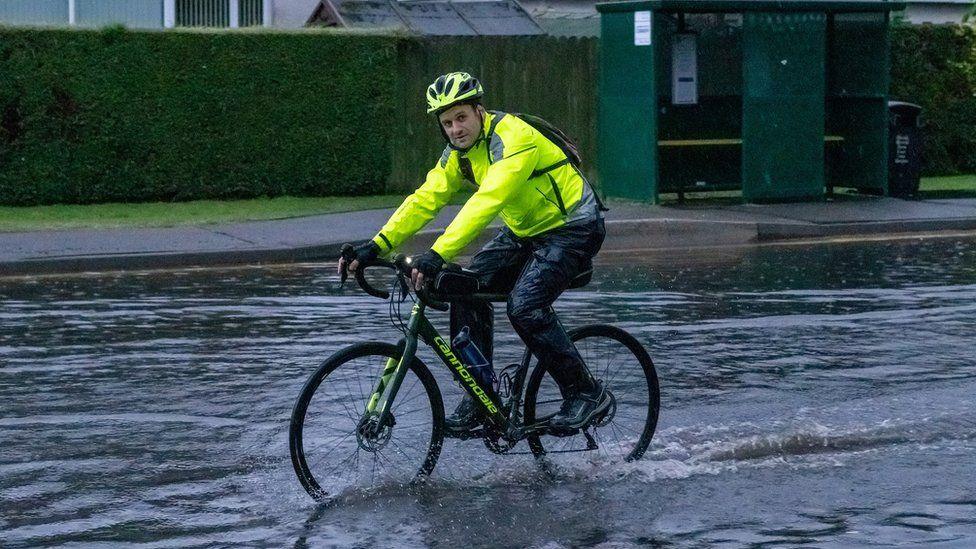 A man in high-vis rides his bike through the water.