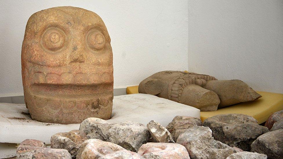 A large stone head and a torso of the God pictured on display