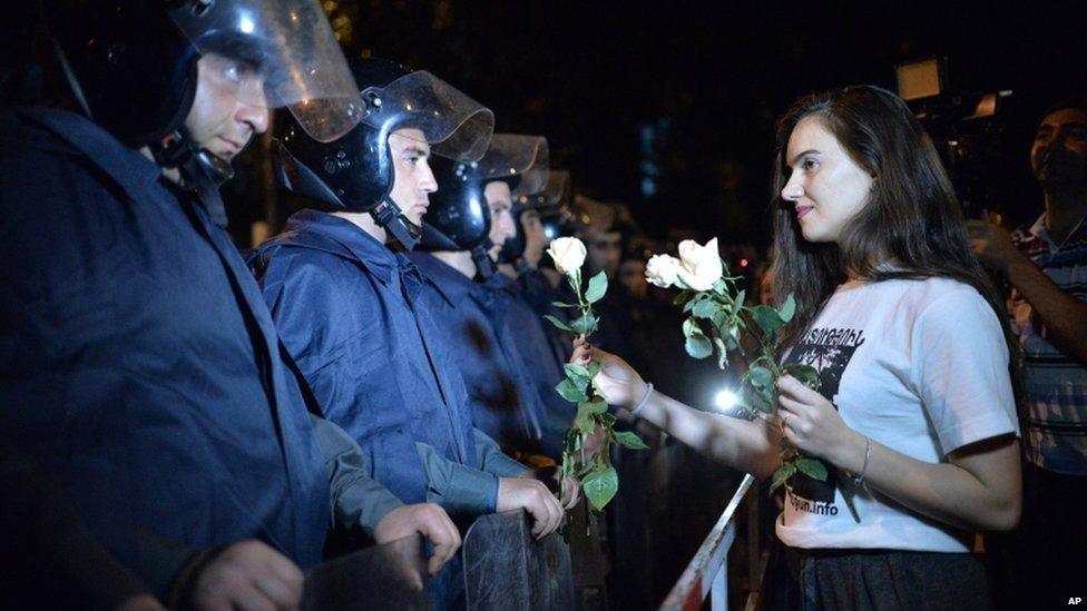 A protester gives a white rose to police officers during a protest rally against a hike in electricity prices in Yerevan, Armenia, Friday, 26 June 2015