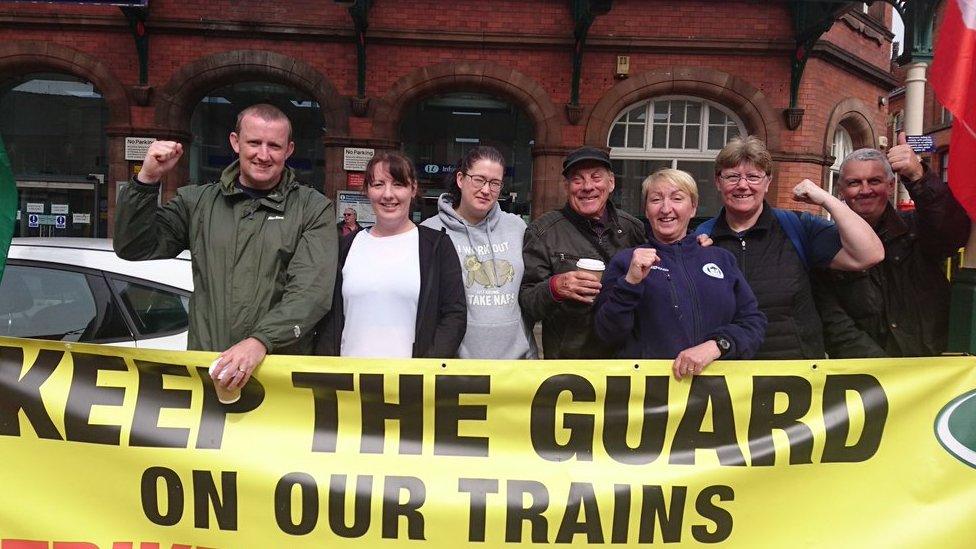 People waving banners at a picket line in front of a train station