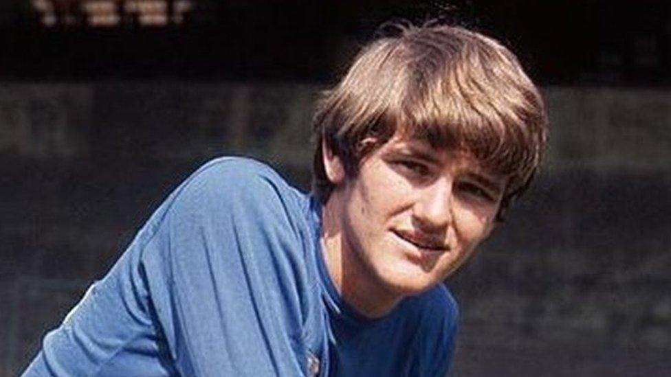 Trevor Whymark in a blue Ipswich Town shirt and white shorts. He is kneeling on a football pith