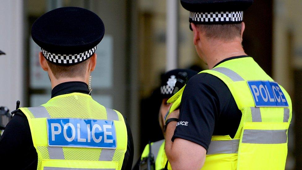 File photo showing the backs of two anonymous uniformed police officers talking to colleagues.