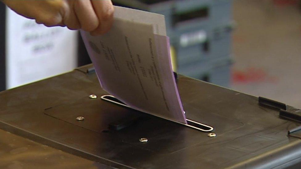 Someone putting a voting slip in a ballot box