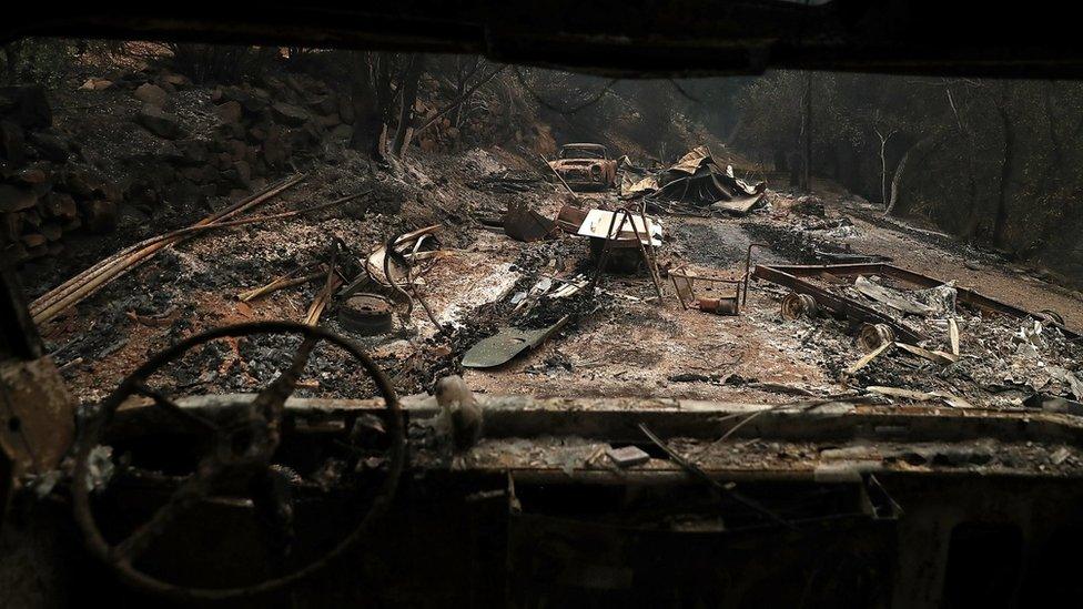 Scorched road viewed through the windscreen of a burnt out car.