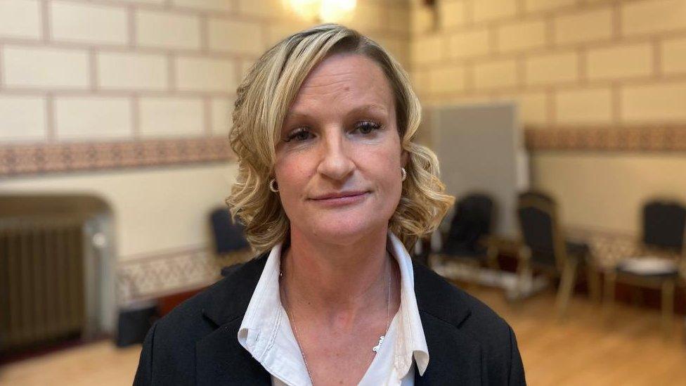 Woman with medium-length blonde hair standings in a council building