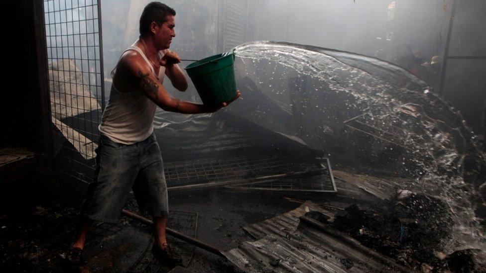 A man uses a bucket of water to help extinguish a fire at the oriental market,