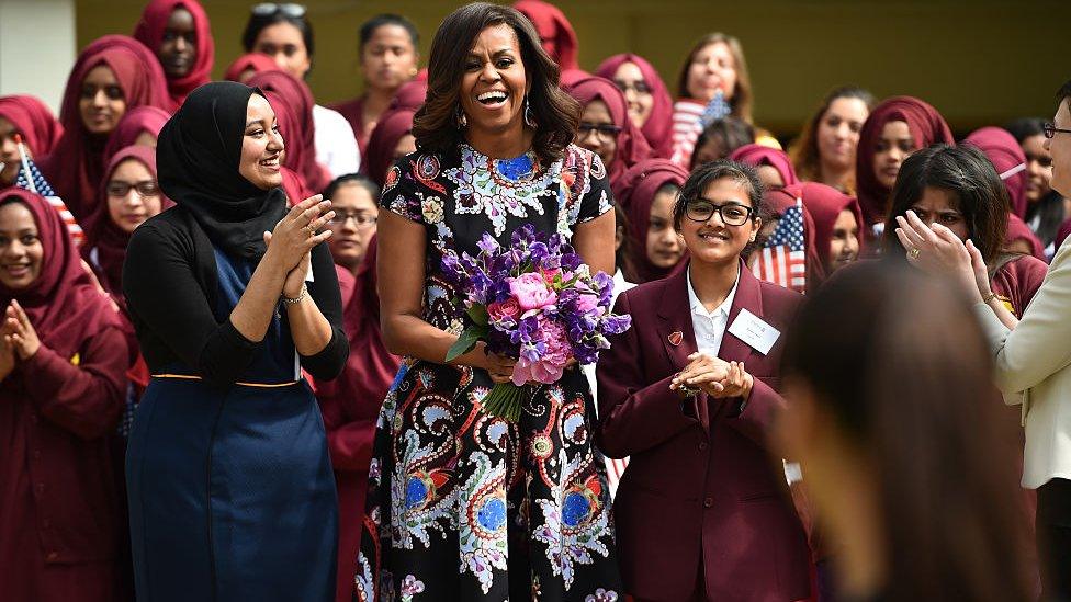 S First Lady Michelle Obama holds flowers as she is received by young students holding the American flag in the courtyard before an event as part of the 'Let Girls Learn Initiative' at the Mulberry School for Girls on June 16, 2015 in London,