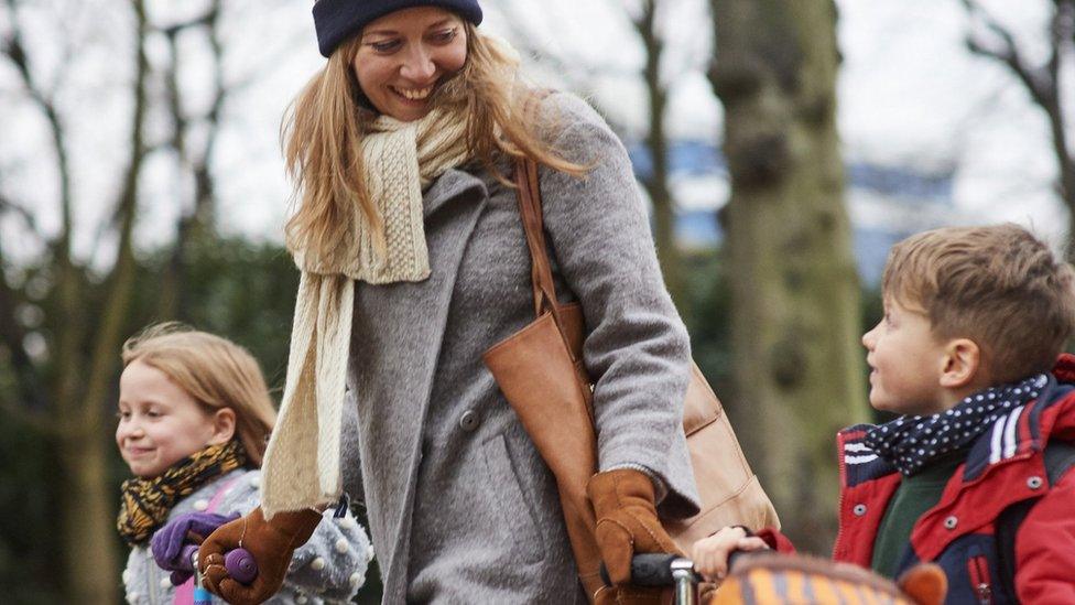 Young mum walking her children from school with their scooters, on cold autumn afternoon (stock photo)