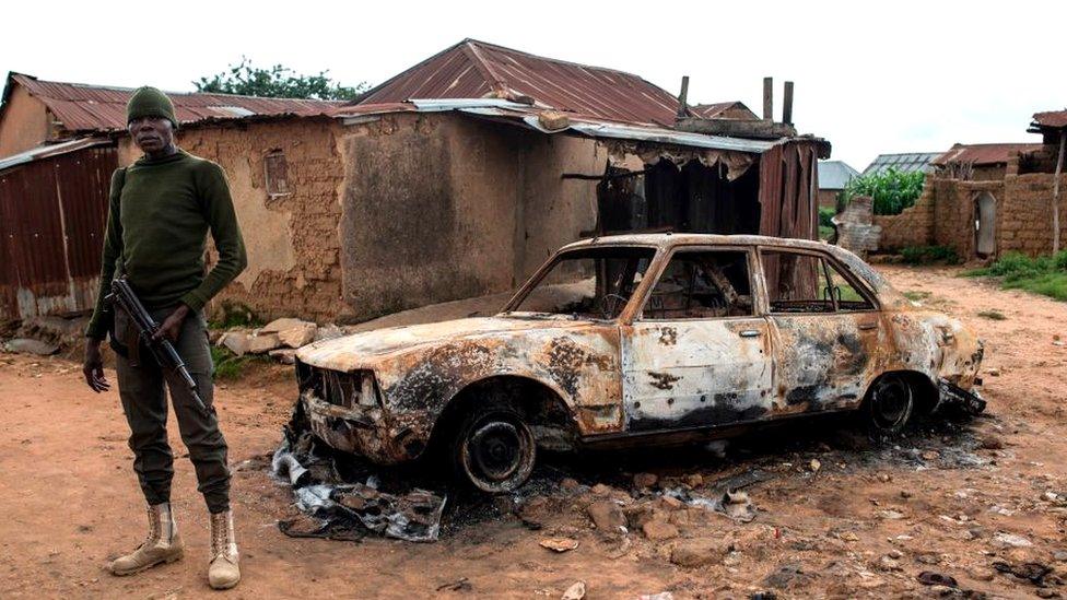 Soldier standing near a burnt-out car