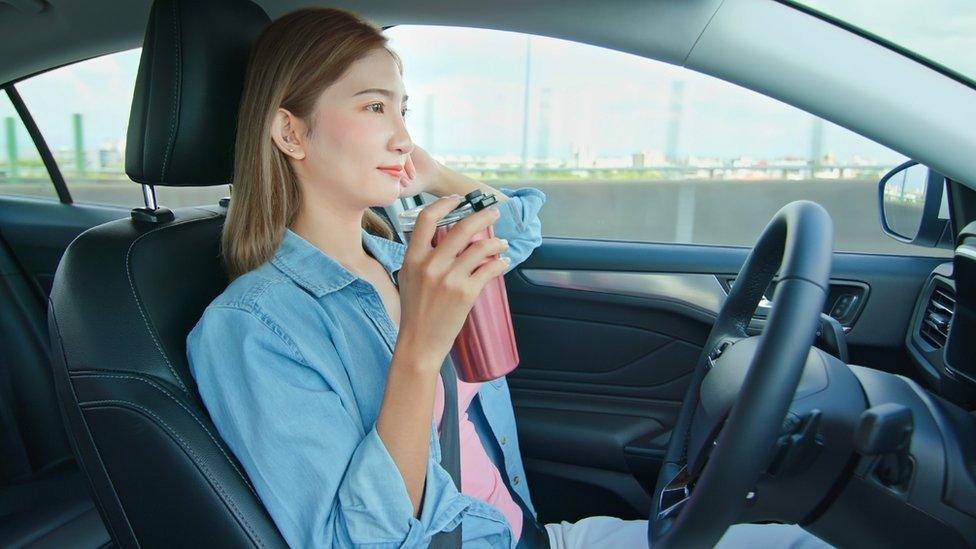 Woman drinking a coffee while sitting behind the wheel of a self-driving car