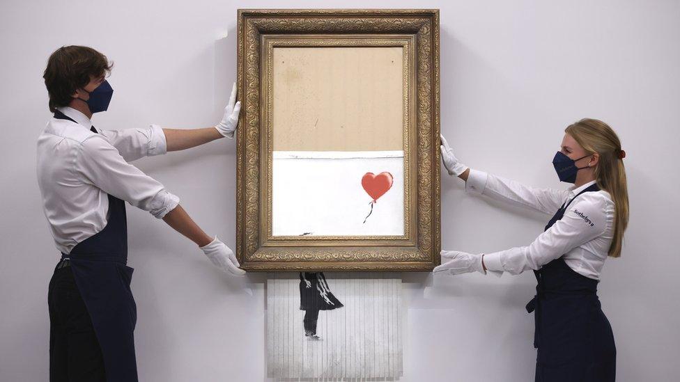 Gallery employees pose for photographers next to a painting entitled "Love is in the Bin" by anonymous British street artist Banksy at Sotheby's auction house in London,