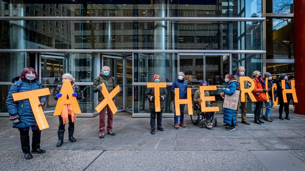 Protesters hold signs saying tax the rich