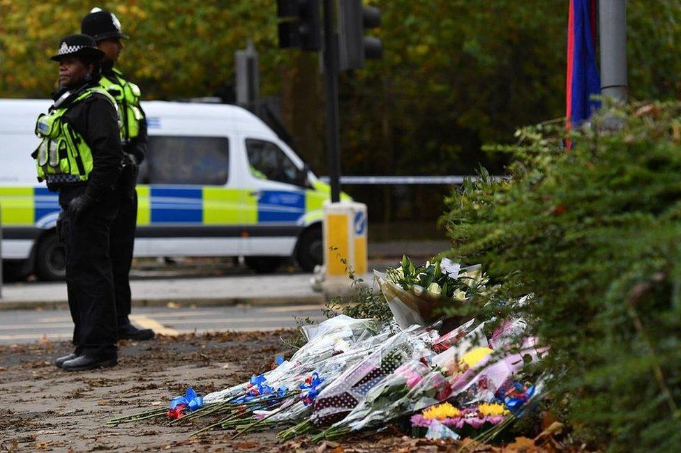 Police stand by flowers left near the scene of a derailed tram in Croydon