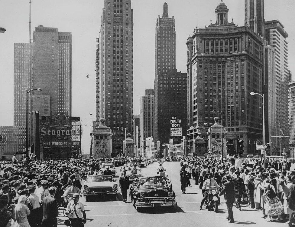 An open top car carries Queen Elizabeth II Prince Philip, Duke of Edinburgh north on Michigan Avenue, with the skyscrapers of the city of Chicago in the background, during a motor trip through the city after her arrival on the Royal Tour, 9 July 1959.