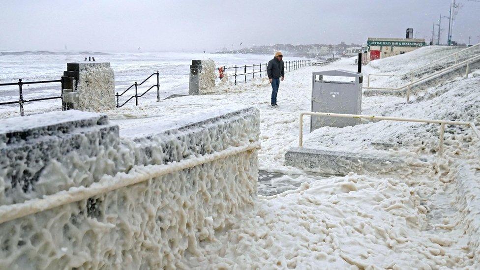 A man walks through sea foam in Seaburn, Sunderland, as Storm Babet batters the country