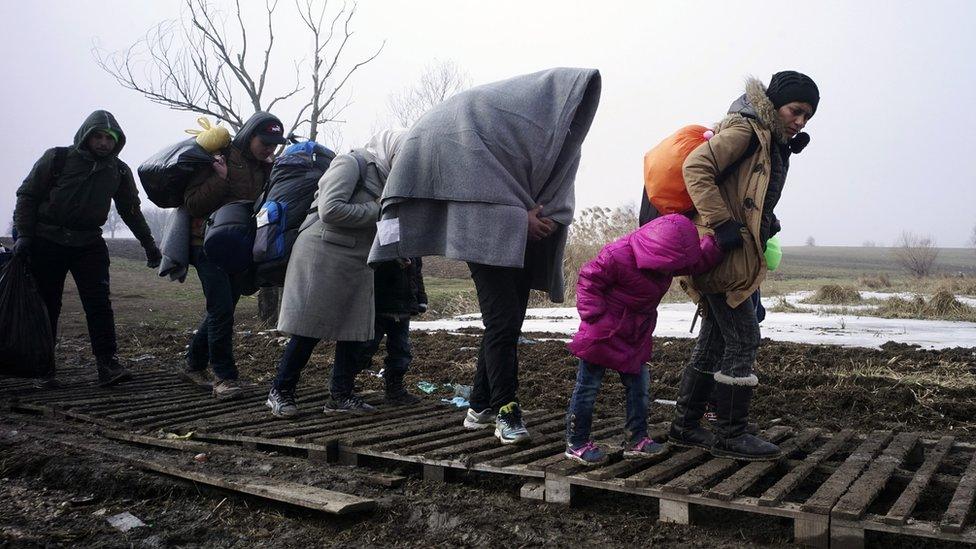 Migrants walk through mud as they cross the Macedonia-Serbia border in the southern Serbian village of Miratovac on 27 January 2016