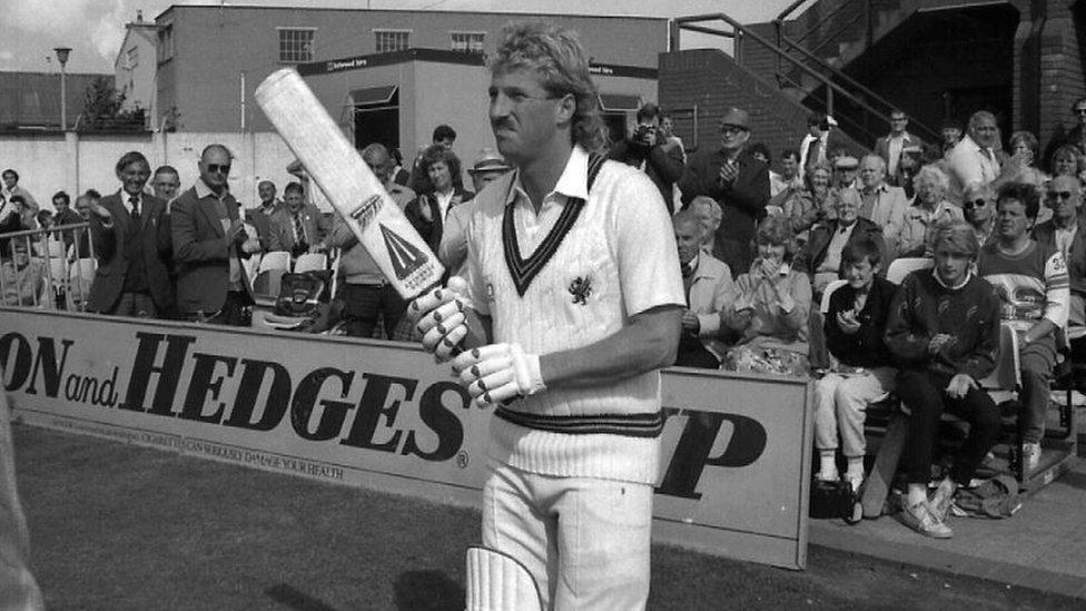 Ian Botham holding a bat on the cricket ground