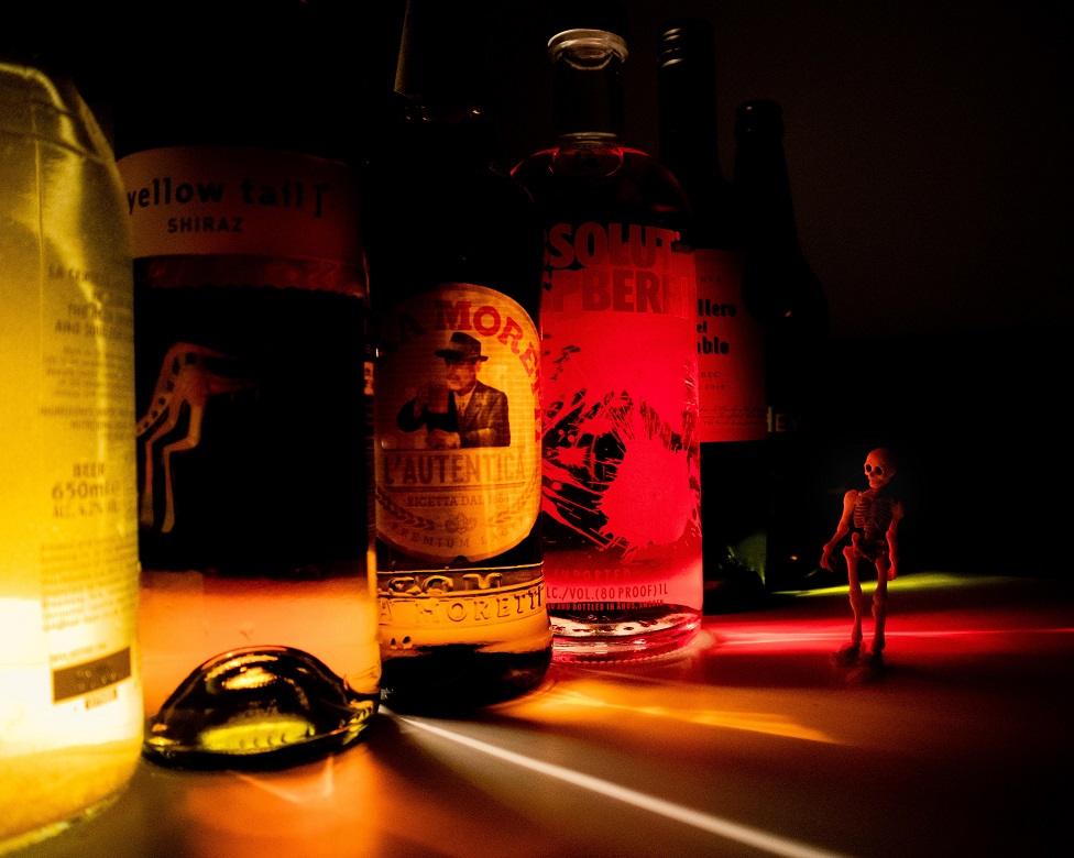 A row of bottles of alcohol with a small skeleton toy