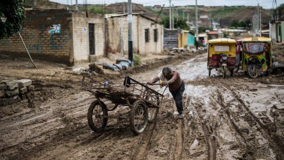 A local resident pushes his cart through the mud after the flooding caused by recent rains, in the province of Paita in Piura, northern Peru, on March 24, 2017.