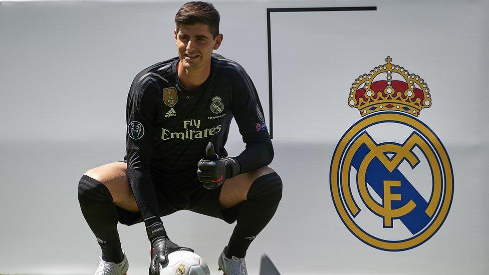 Thibaut Courtois poses next to the Real Madrid logo