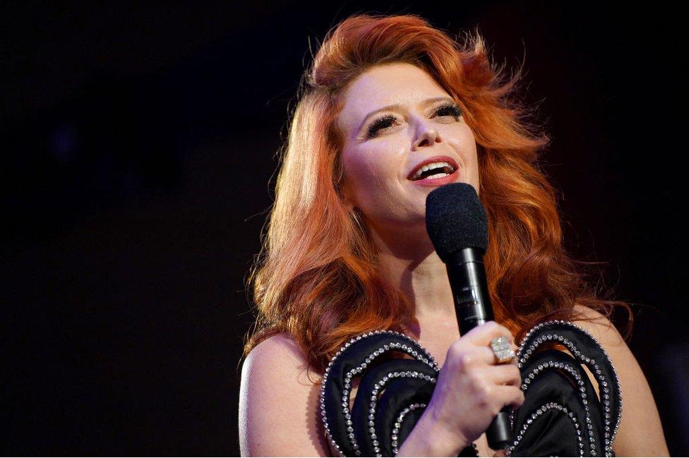 Natasha Lyonne pictured with a microphone in a black dress