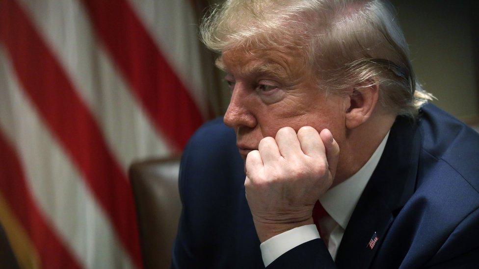 President Trump leaning on his hand with the American flag in the background