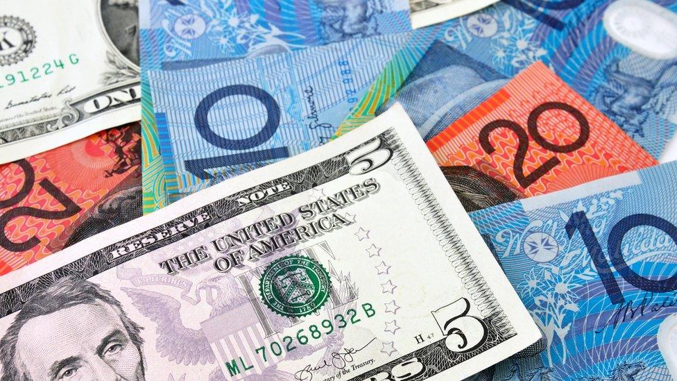 A US $5 note sits on top of a stack of Australian currency