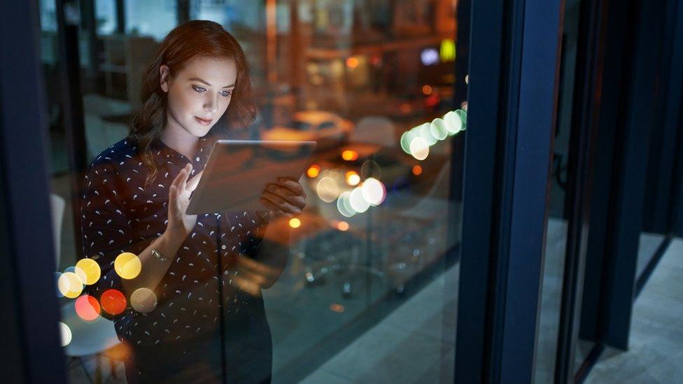 Young woman uses a tablet computer in the office late at night.