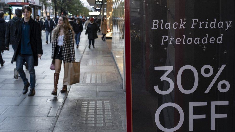 Shoppers in the background of a discount sales board